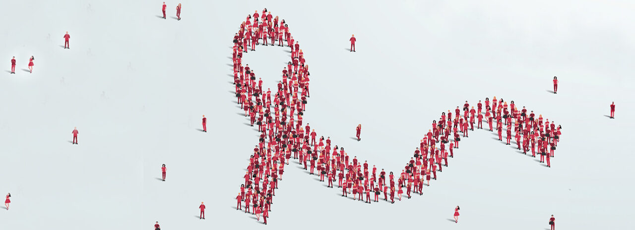 Eine große Gruppe rot gekleideter Menschen steht zusammen und bildet die Form eines Bandes auf einem hellen Hintergrund. Andere rot gekleidete Personen sind um das Band herum verstreut. Eine große Gruppe rot gekleideter Menschen steht zusammen und bildet die Form eines Bandes auf einem hellen Hintergrund. Andere rot gekleidete Personen sind um das Band herum verstreut.