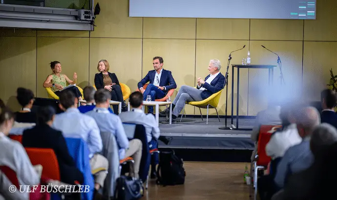 Vier Personen sitzen auf einem Podium vor Publikum.